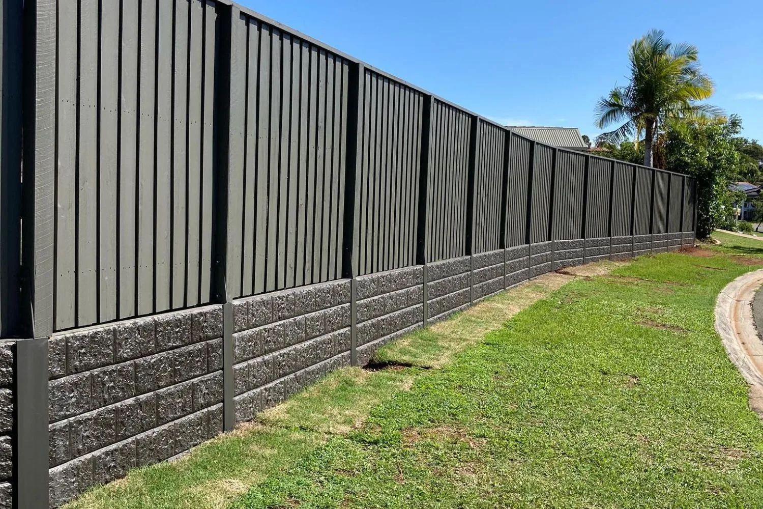 Dark composite retaining wall along a curved street with a palm tree