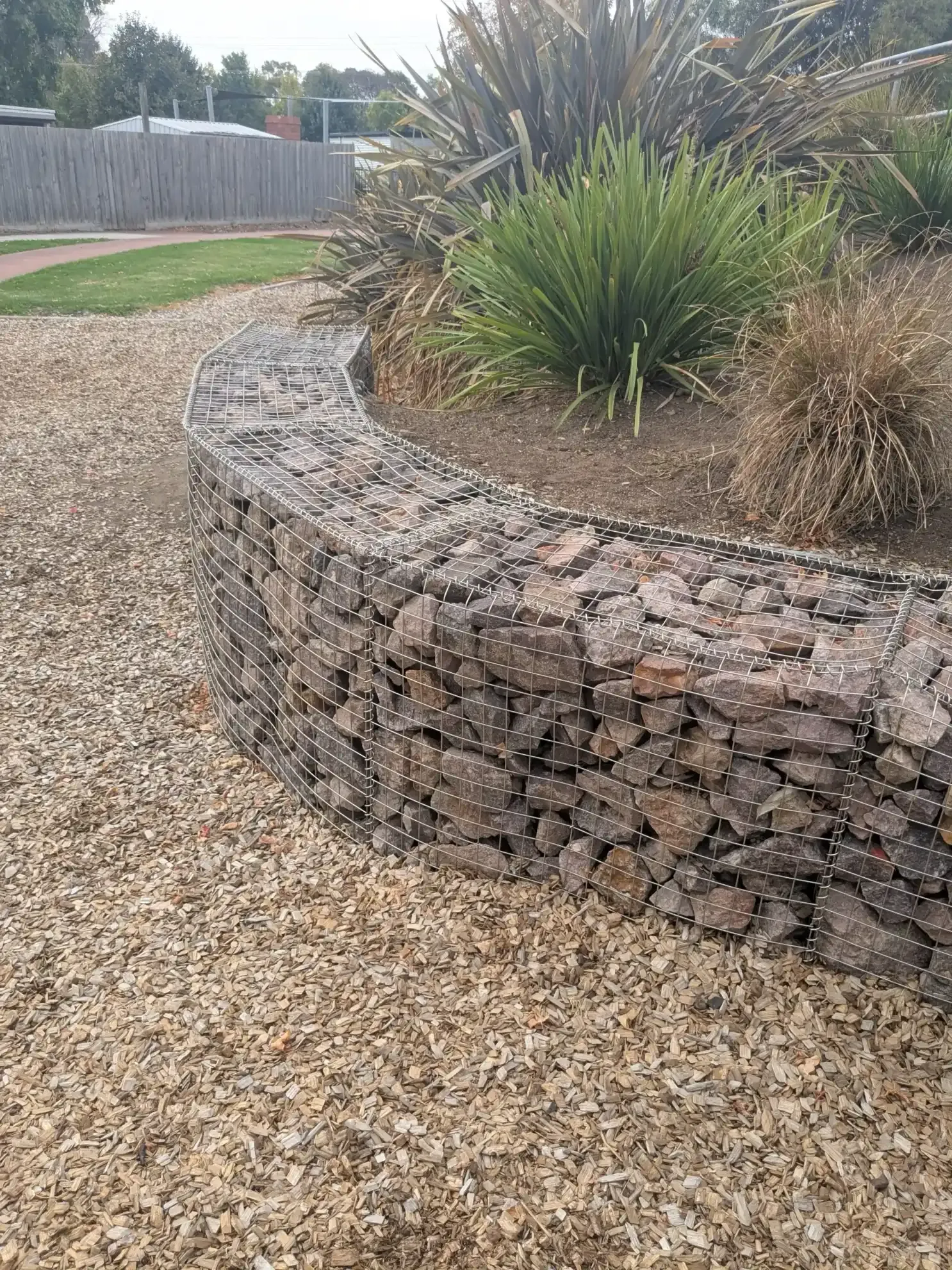 Curved gabion retaining wall beside a gravel path and native plants