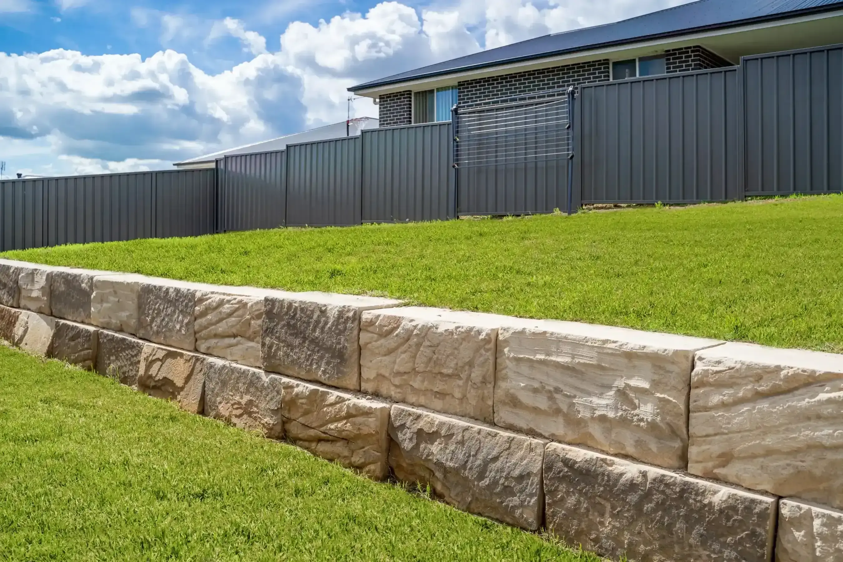 Sandstone block retaining wall along a grassed roadside verge