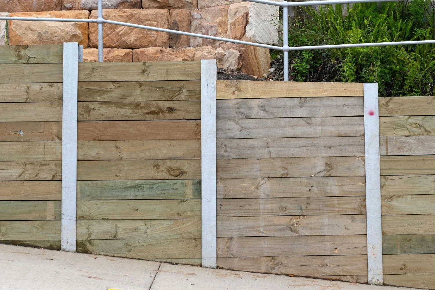Treated pine timber retaining wall along a fence line with established trees